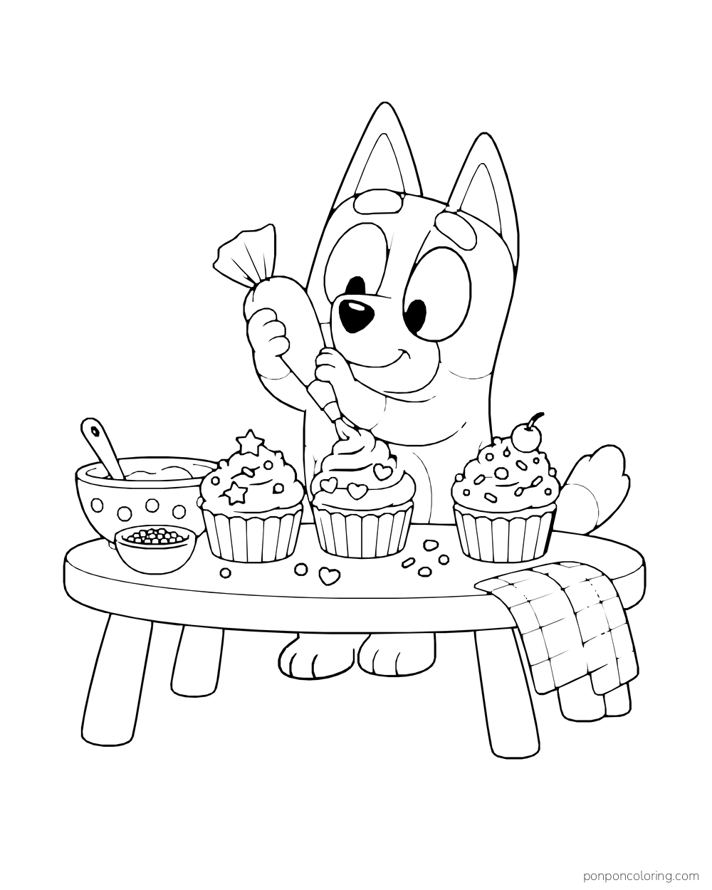 Bingo pipes icing onto cupcakes at a low table with bowls and a folded cloth.
