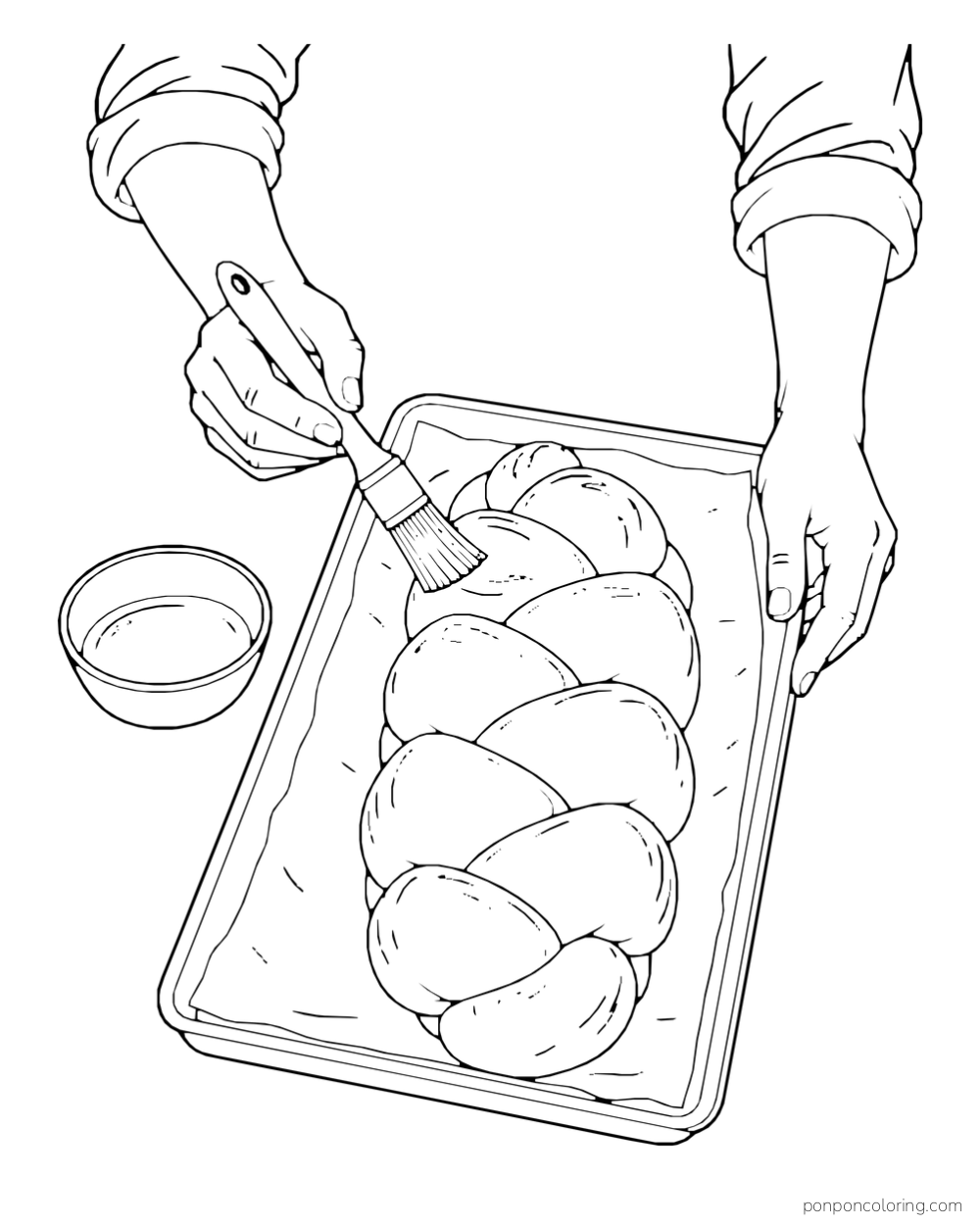 Two hands brush a braided loaf on a baking tray beside a small bowl.