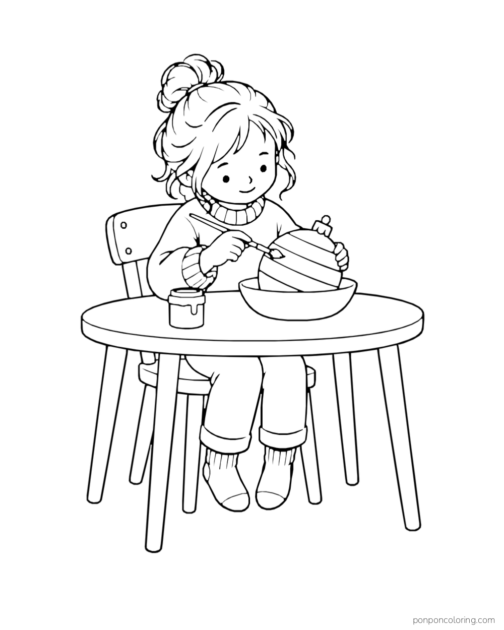 A child paints a striped round ornament resting in a bowl on a table.