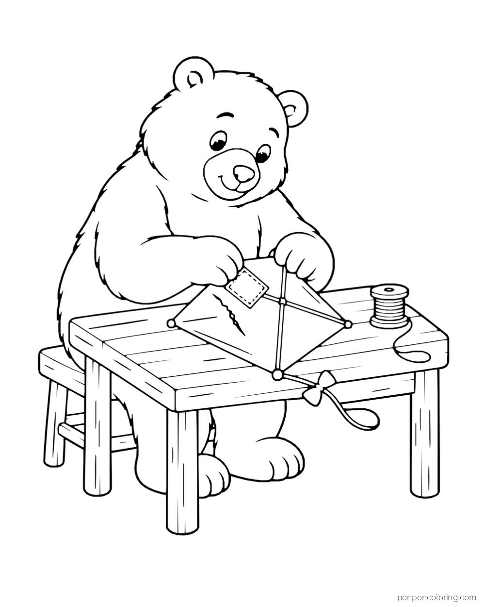 A brown bear presses a patch onto a diamond kite at a wooden table beside a spool of string.