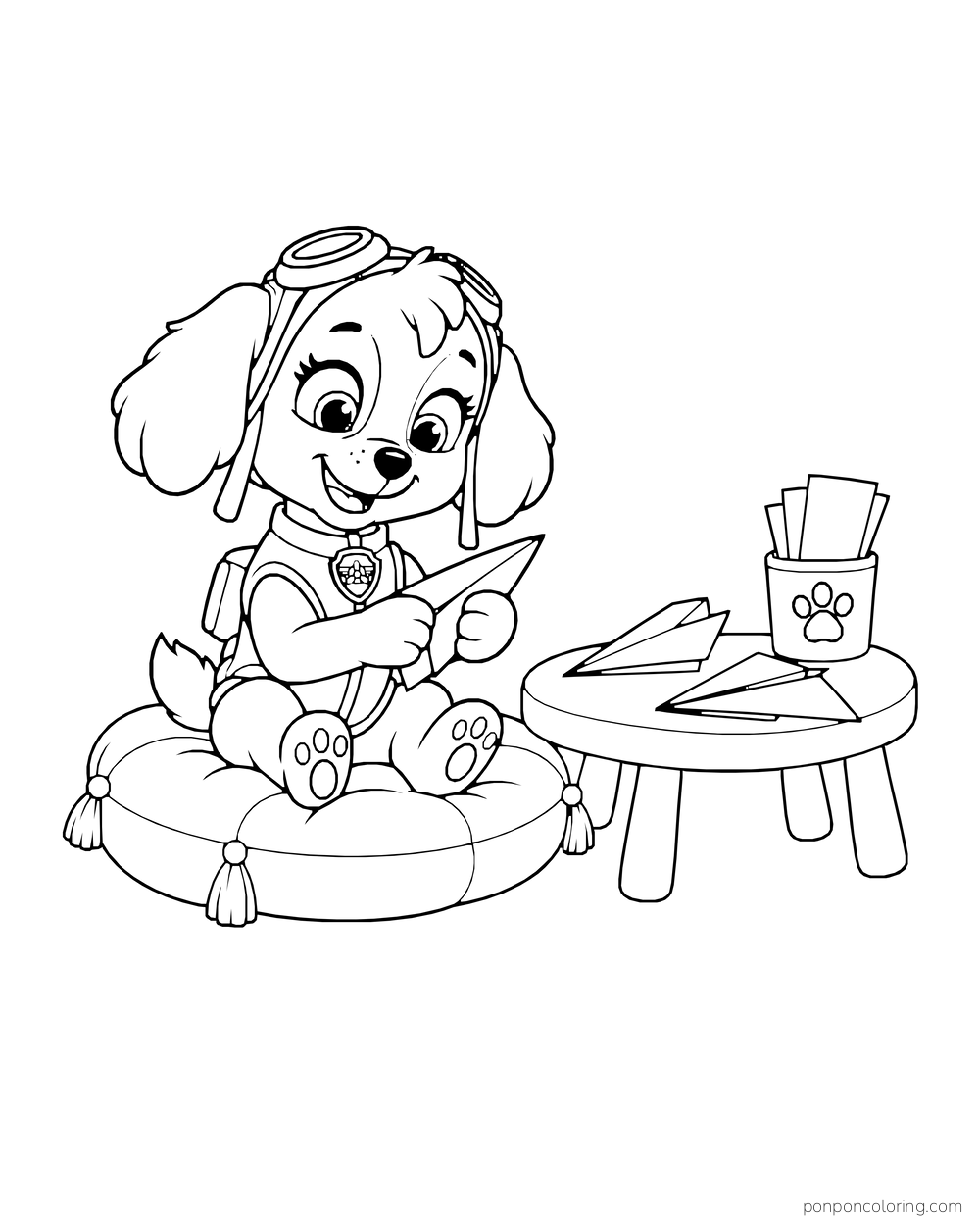 Skye folds a paper airplane on a cushion beside a low table with more planes and a cup of paper.