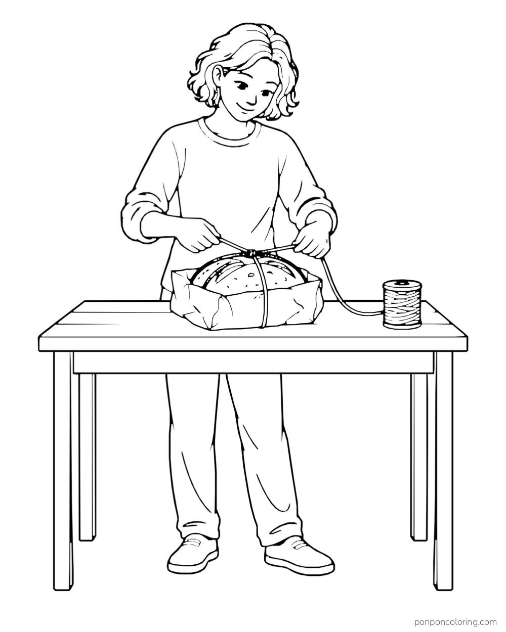 An adult ties string around a wrapped loaf on a worktable beside a spool.